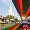 Longtail boat on Bangkok Thonburi canal with white temple on the bank