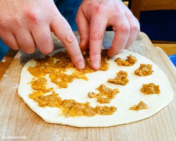 Spreading lamb topping onto dough using fingers